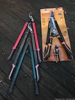 Photo of five yard tools including three pruning loppers, one pink handled pruning shear, and one Fiskars PowerGear lopper in original packaging