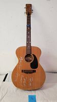 Front view of full guitar showing natural finish, black pickguard, fretboard, headstock, autographs on body.