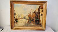 Framed oil painting showing a European street scene with a hotel and pedestrians, signed by artist.