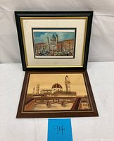 Photo showing both framed art pieces: the signed oil painting on top with Italian architecture and the wooden marquetry art below depicting an Italian cityscape with bridge and dome.