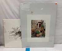 Two lithographs in protective sleeves leaned against a wall, one larger print with beige mount and a smaller print visible behind it.