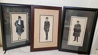 Three framed pen and ink drawings showing full figures in vintage attire, set upright on a table or floor against a white background.