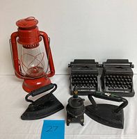 Photo showing red Dietz barn lantern, two cast iron typewriter bookends, three sad irons, and small wood burning stove figurine.