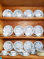 Dinnerware set displayed on wooden shelves, showing arrangement of plates, cups, and saucers with floral pattern.