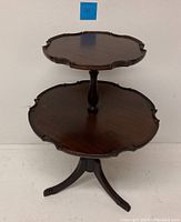 Full view of vintage two-tier mahogany table with pie crust edges and tripod legs.