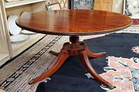 Front view of the round wood coffee table showing the table top and central carved pedestal with four outward curved legs ending with brass horse hoof feet.