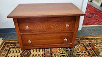 Full view of vintage small wooden chest of drawers showing two drawers and metal knobs on a patterned carpet