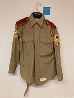 Front view of vintage US Navy khaki uniform shirt showing Legion of Honor patches on sleeves and red shoulder epaulettes with gold piping.