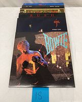 Top view of vintage vinyl records stacked showing several album covers including David Bowie, Steely Dan 'Aja', Rush, and Styx.