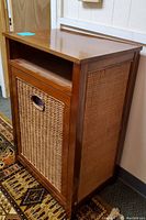 Full side-front view of the wood and wicker hamper showing woven wicker front with handle cut-out and side woven panels.