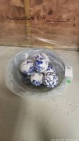 Clear decorative art glass bowl holding six white porcelain decorative balls with blue floral designs, displayed on a flat surface.