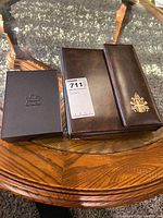 Three coin case boxes: black box with a maple leaf emblem, brown leather case, and a brown leather case with Vatican emblem on top.