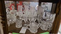 Shelf display of various cut crystal glasses and bowls, including champagne flutes, liqueur glasses, a lidded bowl, sugar bowl, and creamer.