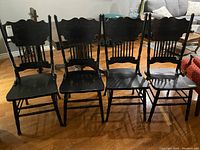 Group of four black wooden dining chairs side by side on hardwood floor