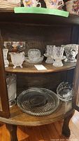 Glass and crystal dishes including serving plates, bowls, candle holders on wood curved shelf