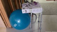 Photo showing blue Fit Circuit exercise ball, silver metal bath stool with rubber tips, and single purple hand weight placed on stool.