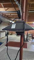 Hanging radiant heat lamp suspended from ceiling with chain and attached black power cord and remote control, in a basement setting.