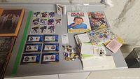 Overview photo of all items on table including hockey cards, pins, stamps, Mad Magazine, and Spiderman comic.