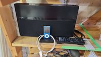 Pioneer sound system with black finish, iPod dock in front with blue iPod Nano, black remote control beside it on wooden shelf