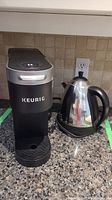 Keurig K900 coffee machine and PC705 cordless kettle shown side by side on granite countertop.