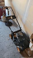 Full side view of black and orange Poulan Pro 675 Series lawn mower with handle and wheels, placed indoors on concrete surface