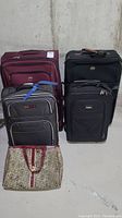Front view of tote bag, three carry‐on suitcases and two larger suitcases arranged on concrete floor