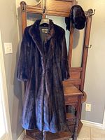 Full view of dark brown mink fur coat on hanger with matching hat on stand
