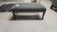 Side view of the rectangular ottoman showing striped fabric upholstery and turned wooden legs.