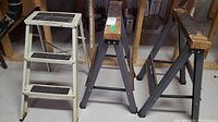 Wide view of two metal saw horses and one white two-step folding ladder on basement floor