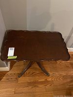 Top-down view of the vintage wooden side table showing scalloped edges and wood grain surface with auction label.