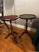 Two vintage pedestal side tables with dark wood bases and scalloped-edged tops with leather inlay.