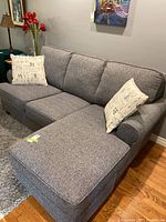 Right-front angle view of grey sofa with chaise on right, two throw pillows