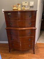 Front view of the dresser showing six drawers with curved fronts and metal ring pull handles, polished wood finish.