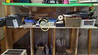 Shelving unit holding multiple tools including a plastic toolbox, small containers, electrical items, and hand tools.