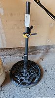 Full view of cast iron umbrella stand, showing round floral base and central pole with yellow-black bird magnet attached.