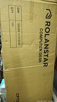 Boxed Rolandstar computer desk with printed dimensions 168x68.1x105cm and model info.