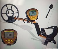 Metal detector assembled showing coil, control box with LCD and foldable shovel leaning.