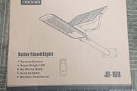 Close-up of Avanfi JD-198 Solar Flood Light box showing remote control and feature list