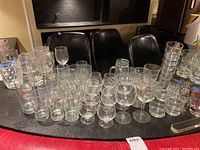 Wide shot of assorted glassware including juice glasses, wine glasses, and commemorative glasses arranged on a table.