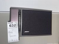 Photo of one Bose speaker with black fabric front next to a note indicating '2 Bose Speakers'. Shows the overall shape and condition of the speaker.