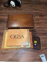 Photo showing three items: monogrammed wooden box with key, Oliva branded wooden box, and brown leather-like case with accessories on wood floor.