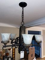 Full view of the chandelier hanging from ceiling showing wooden center and metal arms with glass shades in front angle.