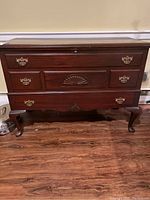 Front view of the wooden chest showing three drawers with brass handles and carved detail on center drawer.