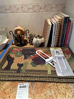 Overall view of the lot showing cookbooks, ceramic jar, glass tea light holder, metal stand, and cabinet locks on a decorative mat.