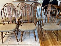 Front view of six wooden dining chairs arranged in two rows showing four side chairs and two armchairs with beige cushioned seats and carved backs.