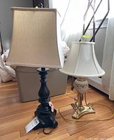 Two table lamps side by side on hardwood floor next to gray storage bin and window letting in natural light