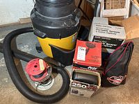 Shop Vac 4.5 HP with hose in foreground, boxed Craftsman portable sprayer, boxed Pete portable sprayer, boxed drain cleaner, and a black and red carrying bag for the portable air compressor