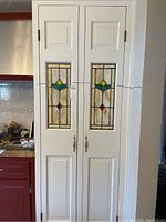 Front view of two tall white cabinet doors installed showing stained glass panels and decorative hardware
