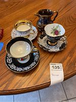 Four bone china items including two Clarence teacups with saucers, one Rosina teacup with saucer, and one Longton creamer displayed on wooden table.