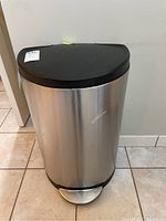Front view of stainless steel trash barrel with black lid and pedal.